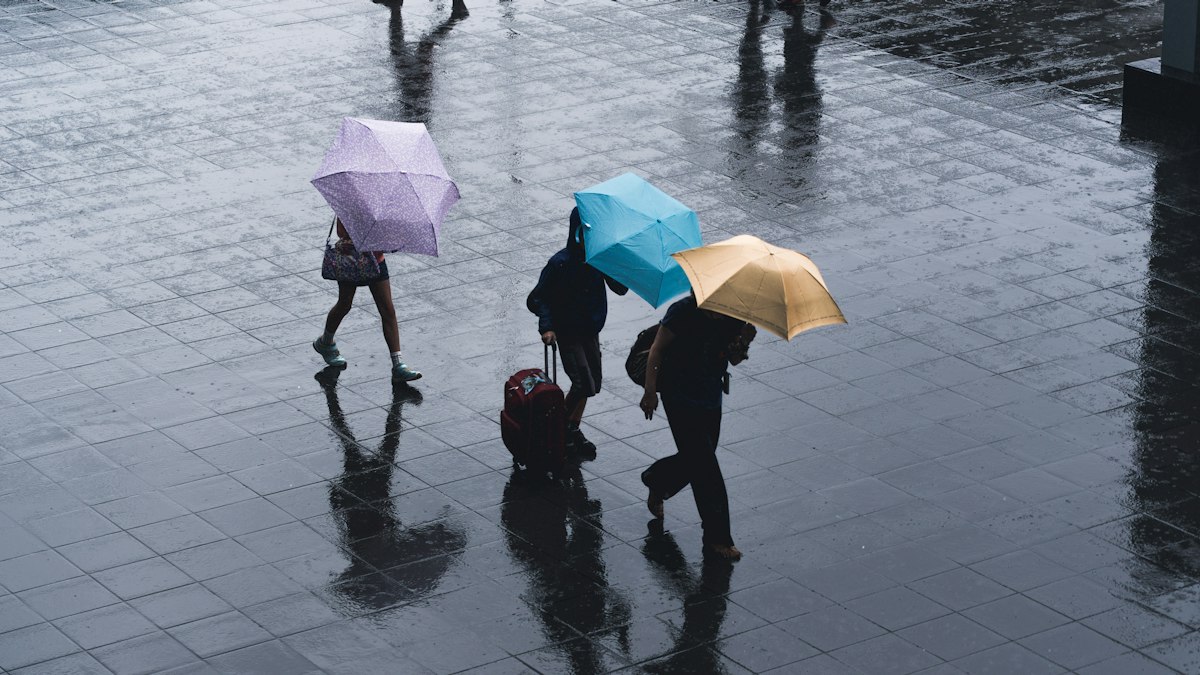 Three people crossing a rain-soaked plaza under colorful umbrellas