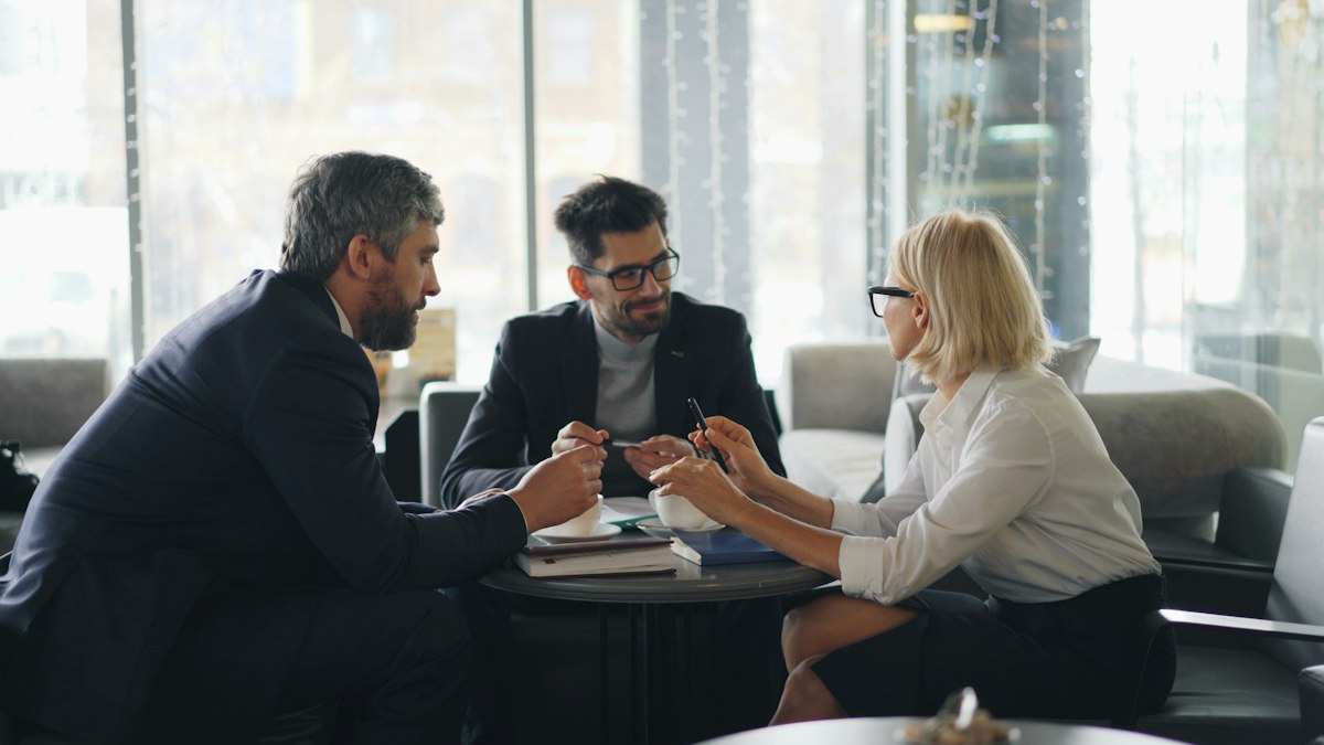 Three people in business clothes talking around a table in a bright office