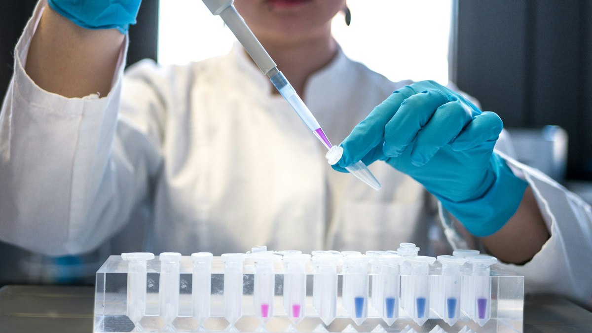 A scientist in blue gloves using a pipette over a rack of test tubes
