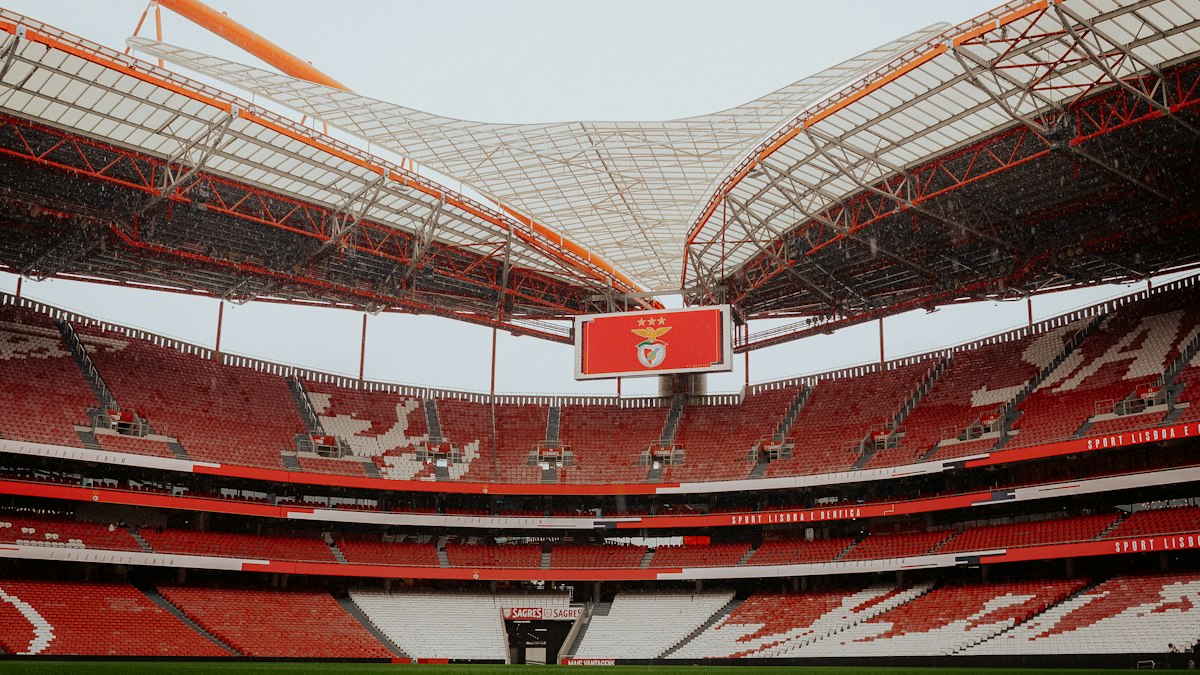 An empty soccer stadium with red seats and a large scoreboard screen