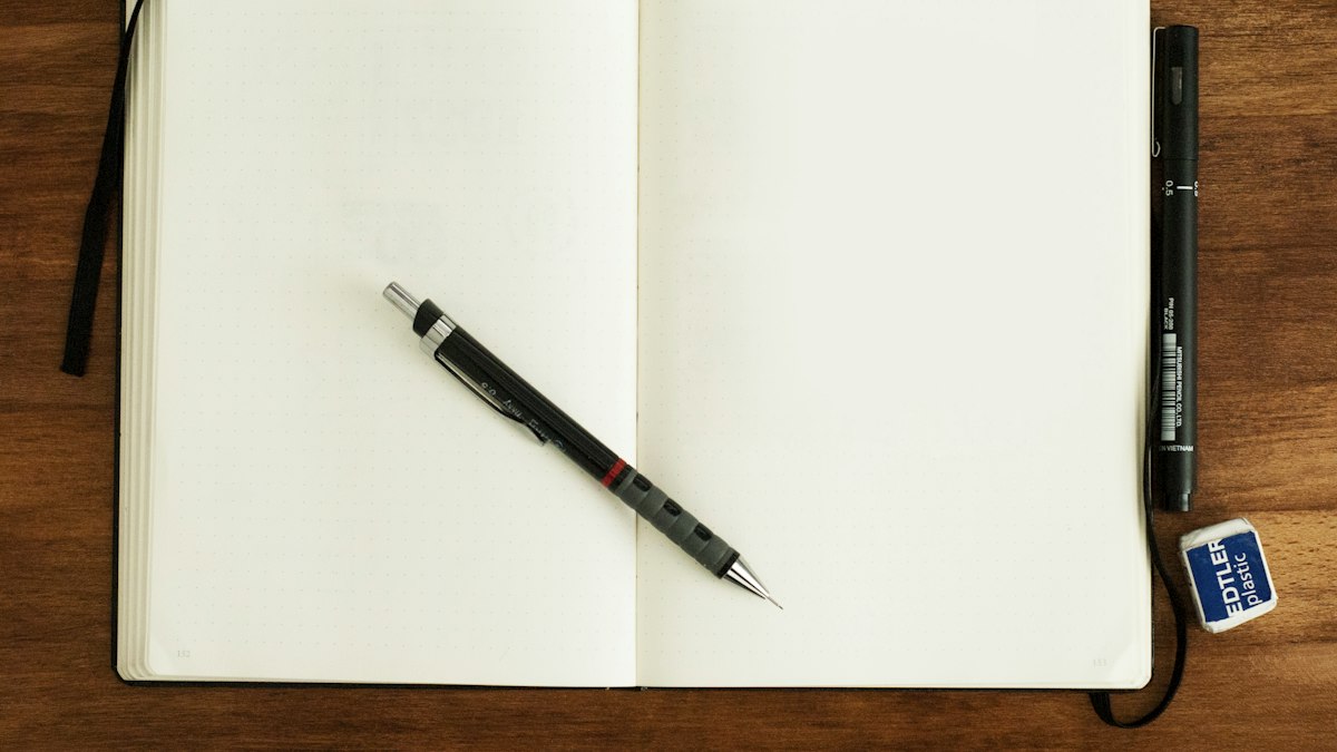 An open notebook with a pen resting on it on a wooden desk
